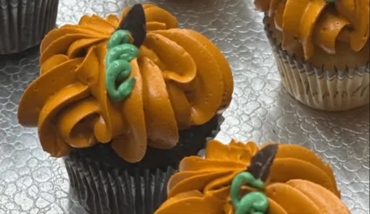 Cupcakes piped with orange buttercream like pumpkins, with green stems