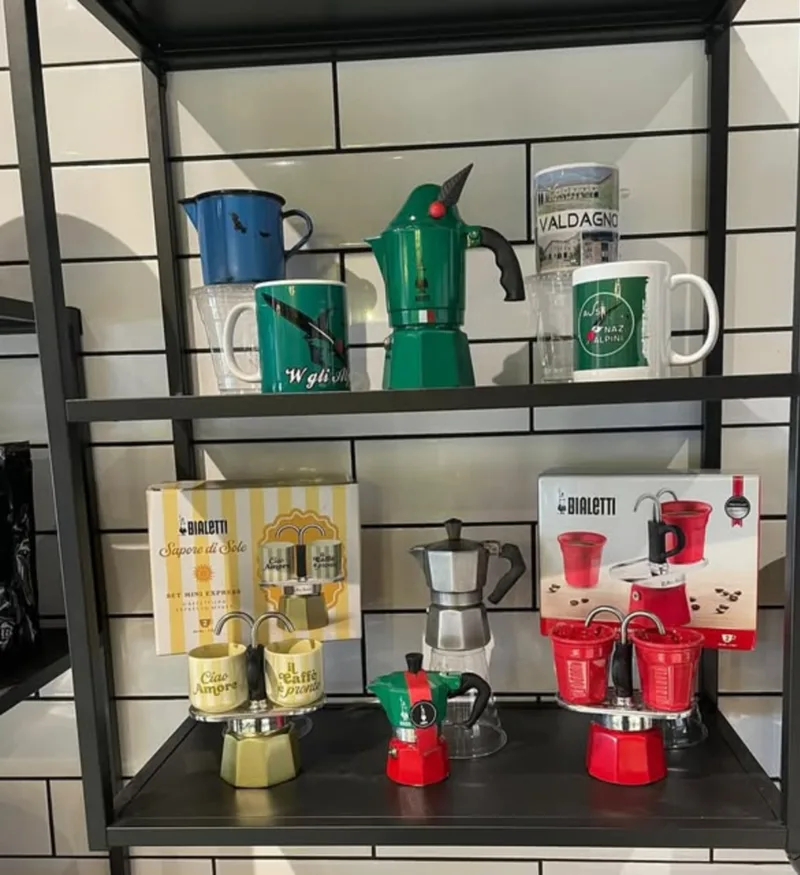 A shelf in the shop with green and red moka pots, espresso cups and mugs